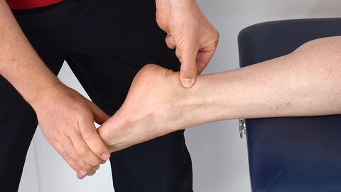 Bildausschnitt: Stehender Mann hält den Fuß eines liegenden und fasst mit einer Hand an den Knöchel