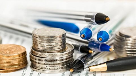 Münzen und Kugelschreiber auf beschriebenem Papier