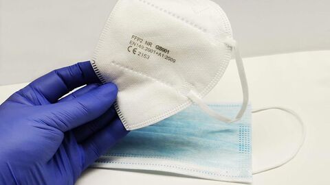 Hand im Gummihandschuh hält eine FFP2-Maske, im Hintergrund liegt eine OP-Maske
