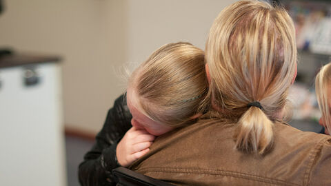 Mutter von hinten mit Tochter, die an ihrer Schulter liegt
