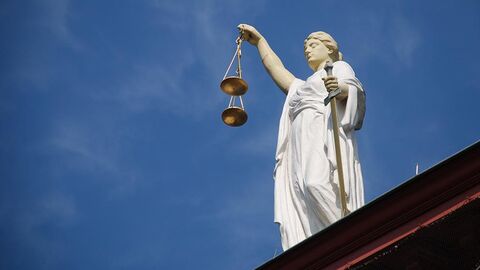 Justitia-Statue steht auf einem Dach vor blauem Himmel.