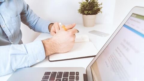 Büroarbeiter Mann sitzt an einem Schreibtisch mit einem Notebook, einer Kladde und einer Topfpflanze.
