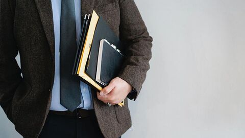 Mann in Geschäftskleidung trägt Akten unter seinem Arm.