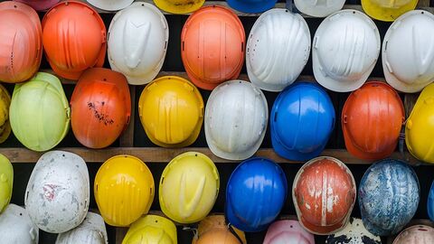 Sicht von oben auf mehrere Reihen verschiedenfarbige Bauhelme.