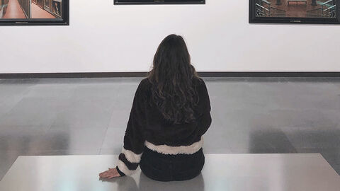 Frau sitzt auf einer Bank in einer Ausstellung und betrachtet Bilder