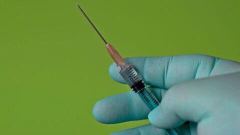 Drei Finger einer Hand halten eine Spritze.